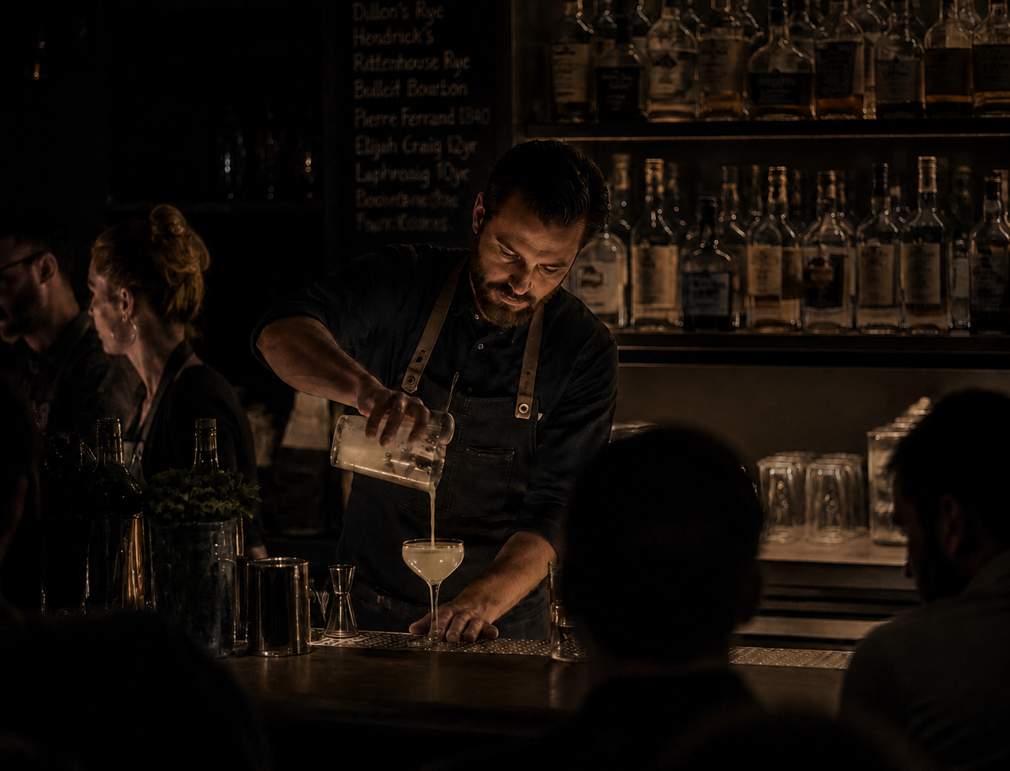 Bartender pouring a cocktail at a low-lit craft bar